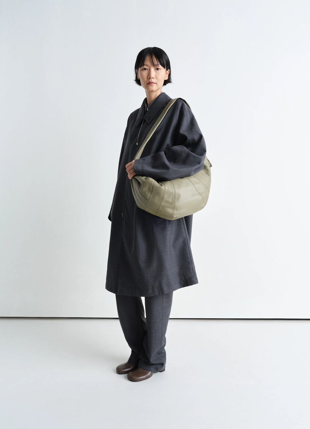 Lemaire large croissant bag in soft grained leather, model shot, three-quarter view worn crossbody overcoat