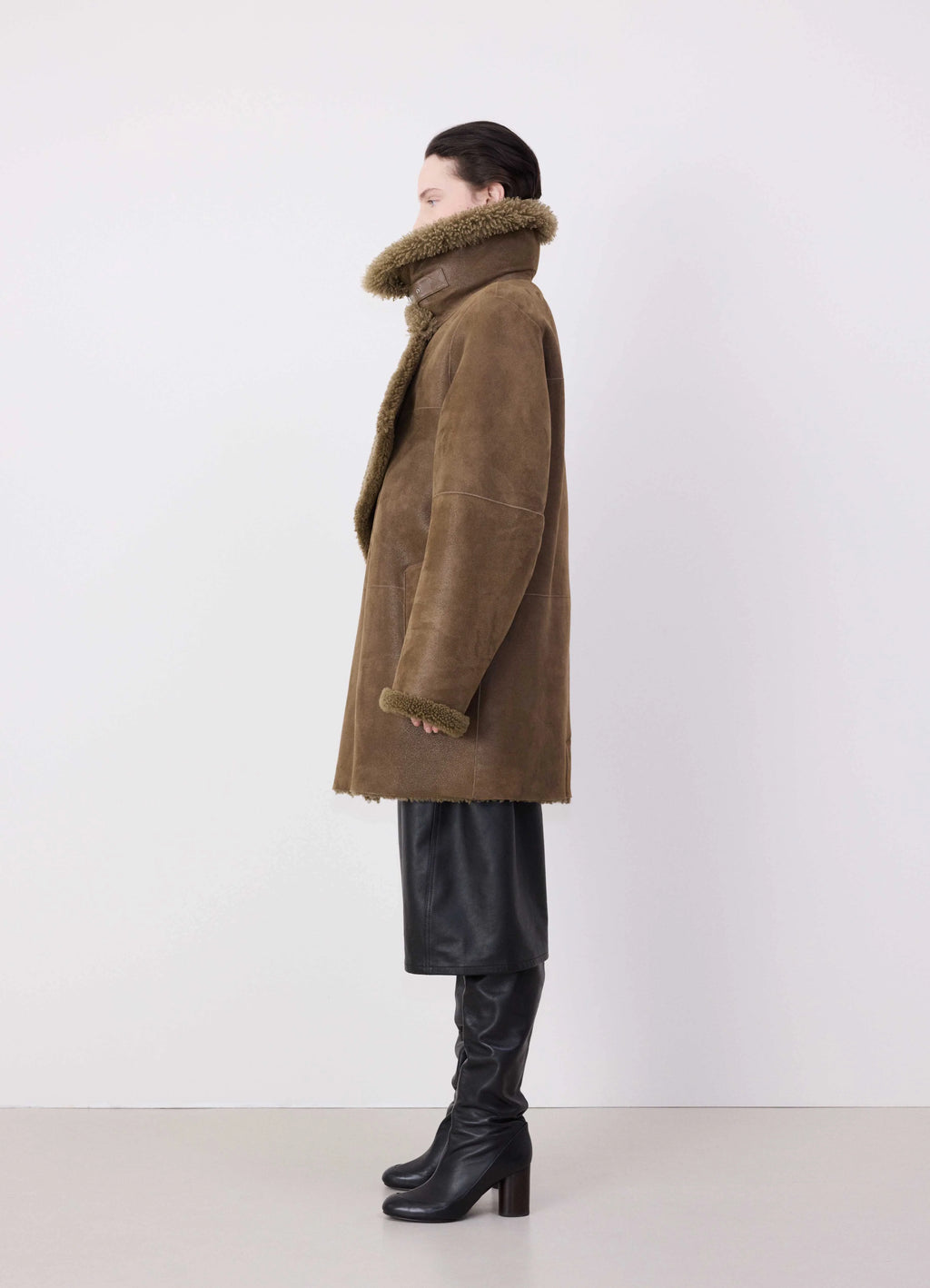 Lemaire asymmetrical shearling coat in curly lamb shearling, grained leath, model shot, side view asymmetrical hem