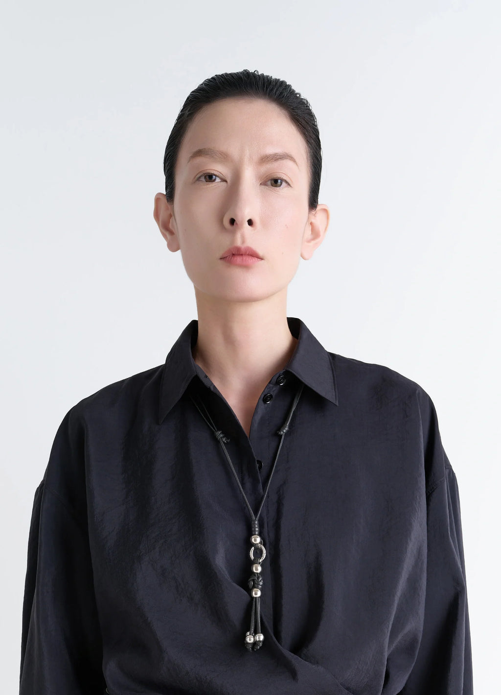 Infinite love knot badge holder in nappa lamb leather, model shot, neckline close-up worn with black shirt