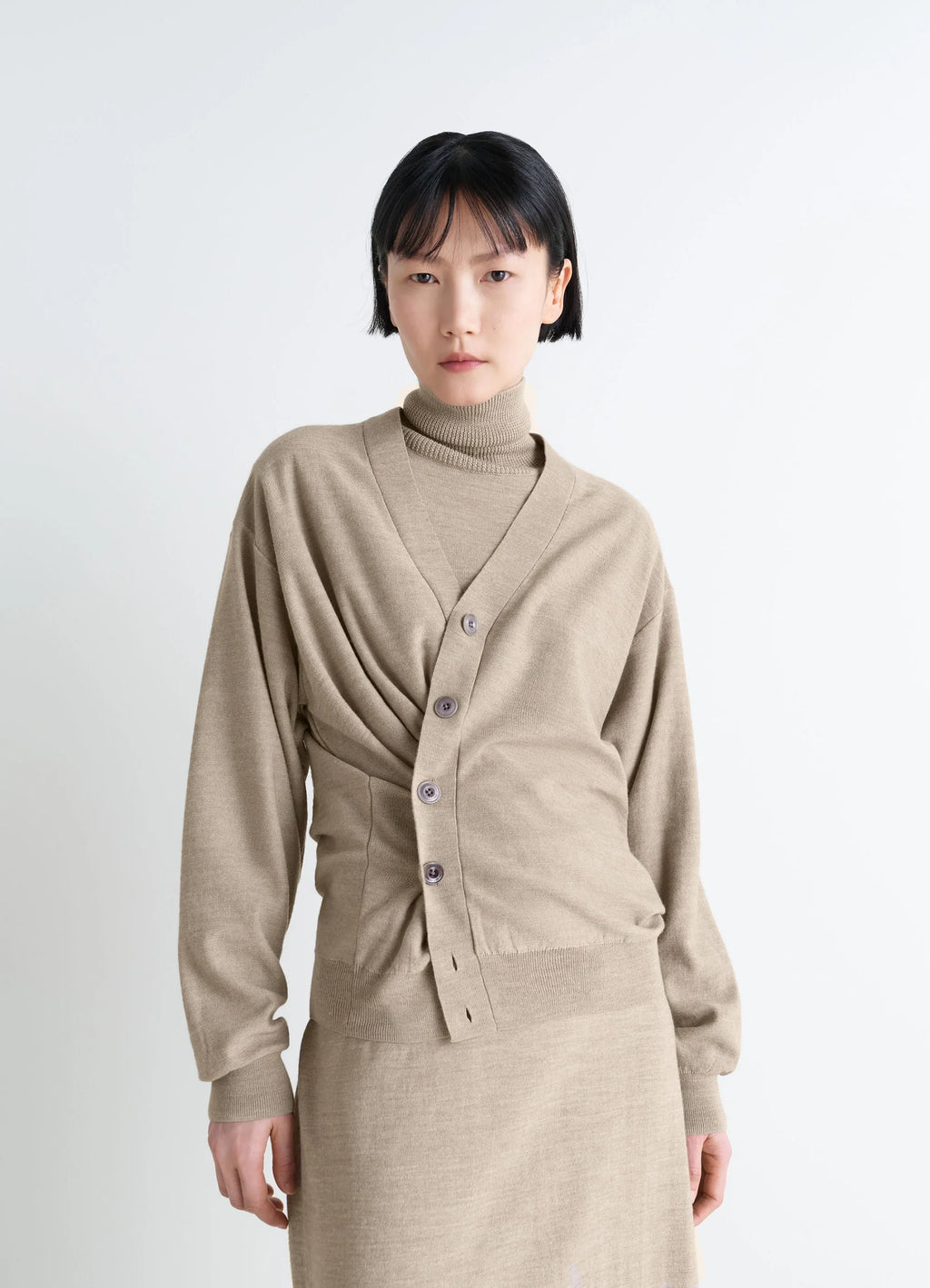 Lemaire relaxed twisted cardigan in light beige blended merino wool, model shot, three-quarter view draped waist detail